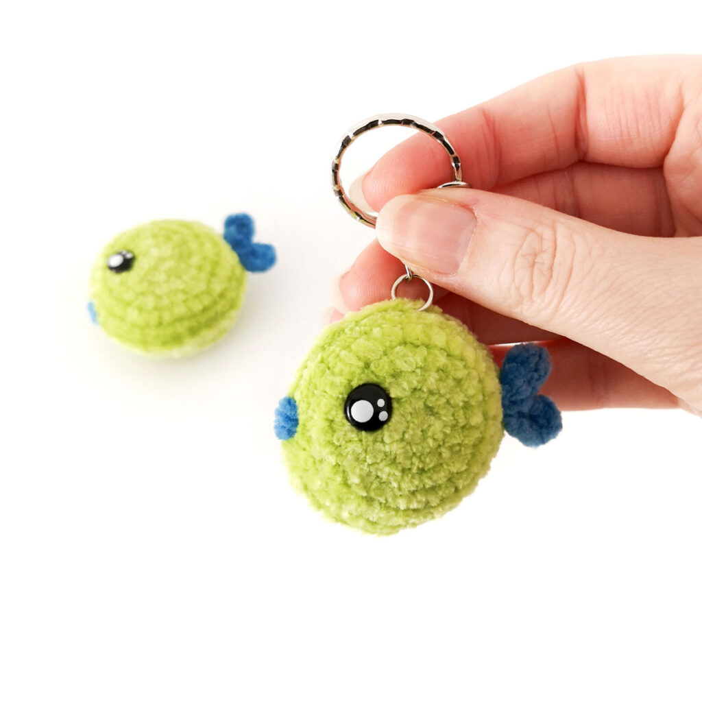 Green crochet fish keychain with a blue tail, held by its keyring.