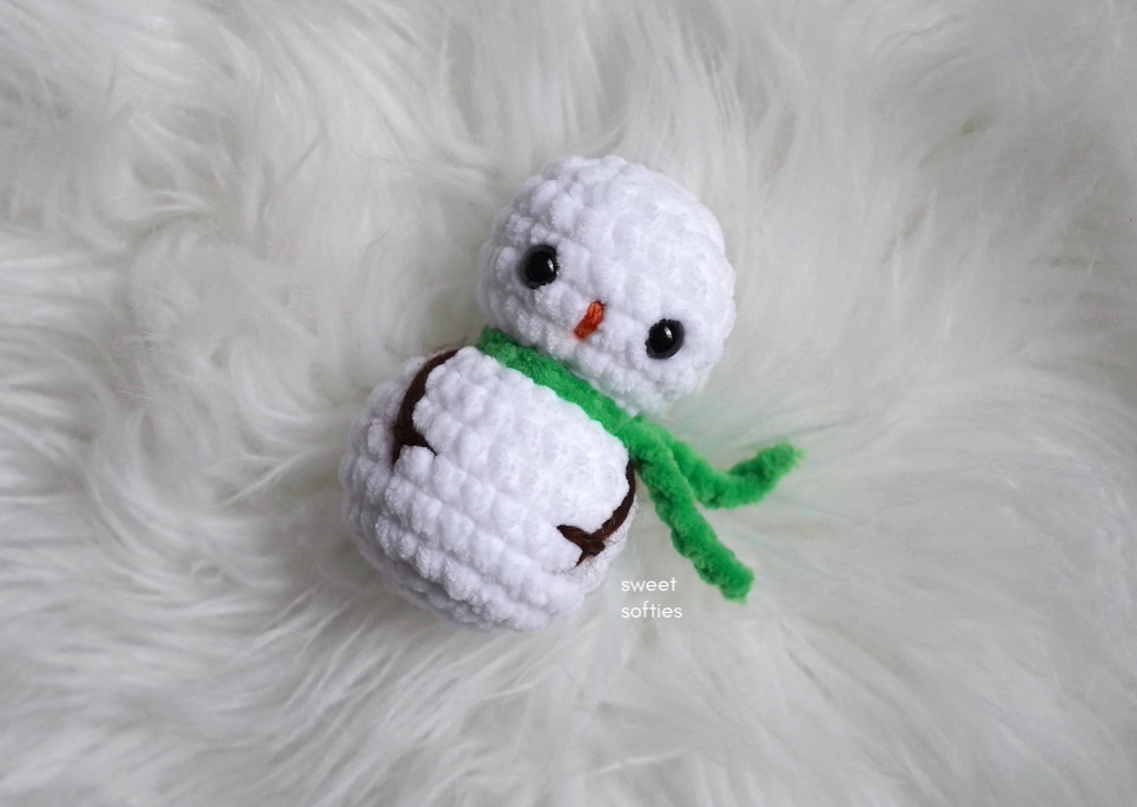 White Chibi crochet snowman with a green scarf and embroidered branch arms by Sweet Softies.