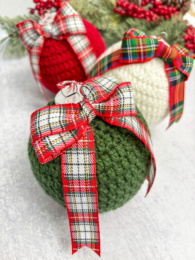 Green, red and cream crochet Christmas baubles decorated with tartan ribbon bows.