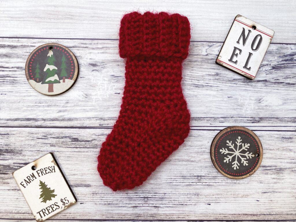 Red mini crochet Christmas stocking with a folded ribbed cuff on a wooden background.