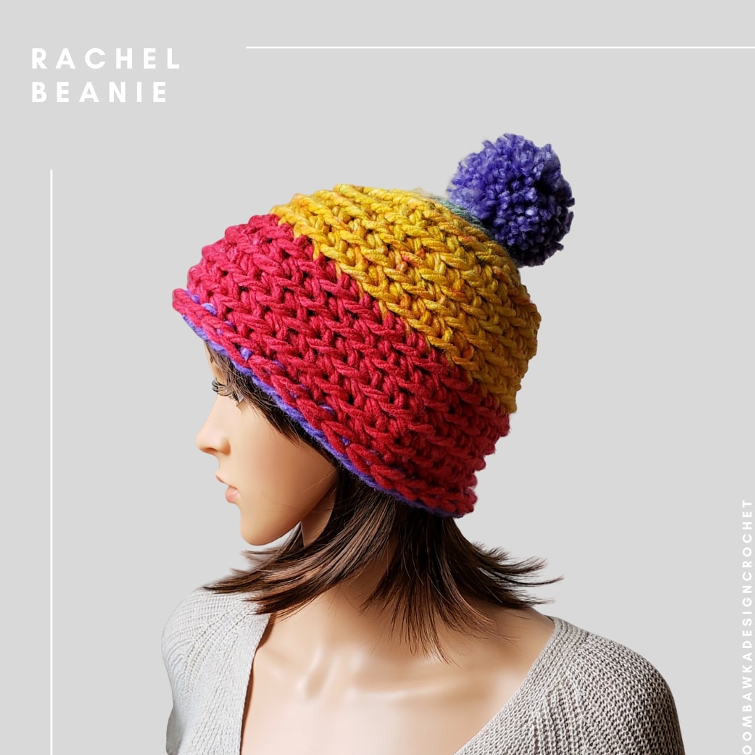 Rachel crochet beanie in red, yellow and purple yarn with a purple pompom, displayed on a mannequin.