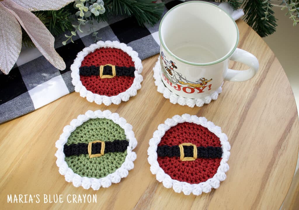 Red Santa and green Elf crochet coasters with white scalloped edges and belt buckle details.